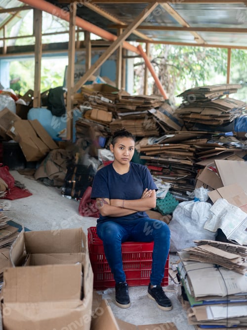 Preview: Young Hispanic Woman Determined Among Cardboard for Recycling in Warehouse. Serious Portrait