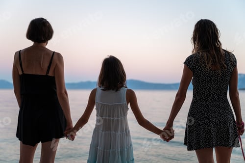 Preview: Lesbian couple holding hands with their daughter in the middle, standing by the sea