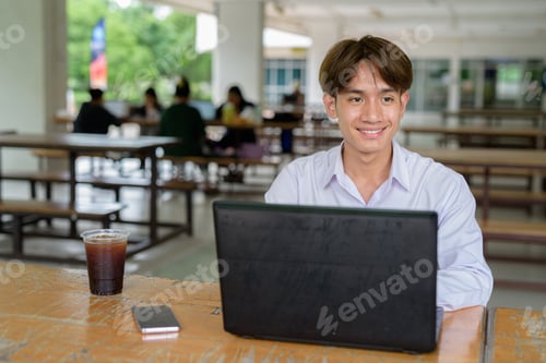 Preview: Non binary university student sitting in college campus using laptop computer
