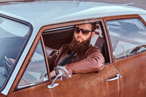 Preview: Bearded male dressed in brown leather jacket and boots with tuned retro car