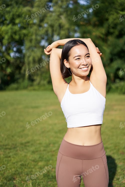 Preview: Asian woman stretching her arms, doing fitness workout in park, smiling pleased, warming up before