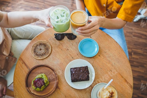 Preview: Hands of teenage girls holding ice green tea and ice coffee with dessert table at cafe.