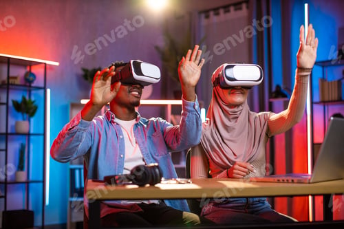 Preview: Young multiethnic couple playing games or working using VR goggles at home
