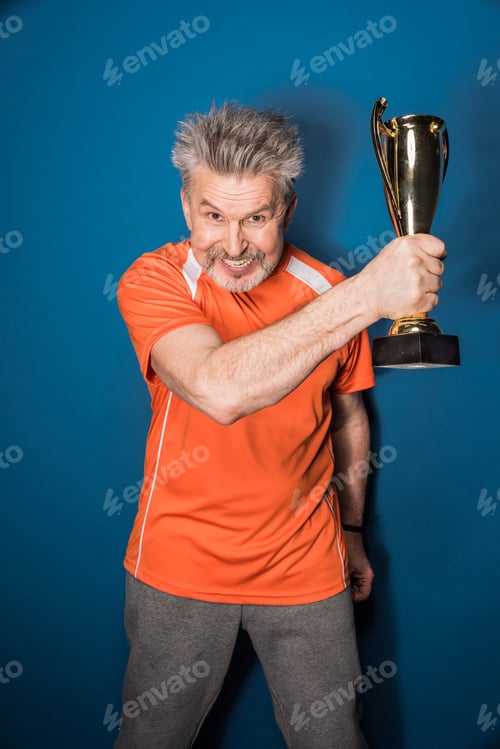 Preview: Excited mature sportsman holding trophy cup isolated on blue
