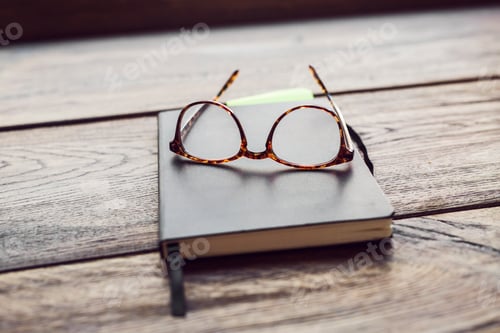 Preview: Eyeglasses and notebook on wooden table