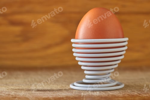 Preview: One boiled egg in a spiral-shaped white metal support on wood background