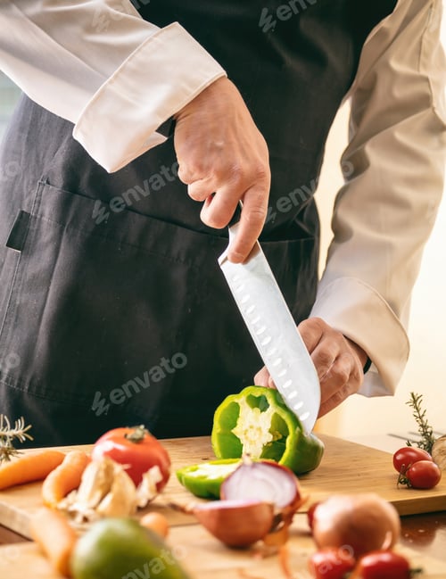 Preview: Chef cut a green pepper with a knife on a chop board, close up. Fresh vegetable on kitchen table.