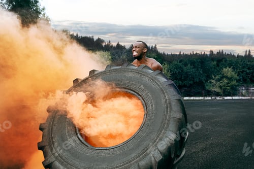 Preview: Handsome muscular man flipping big tire outdoor.