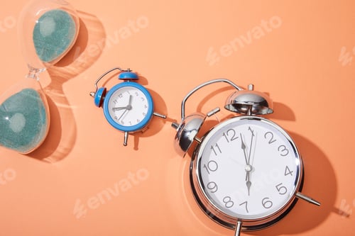 Preview: top view of alarm clocks and hourglass on peach background