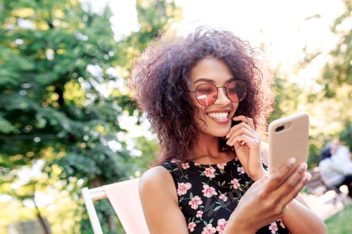 Preview: Mixed race girl sitting on chaise-lounge on lawn and texting message on mobile phone