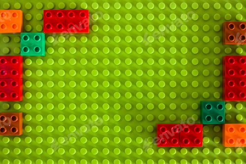 Preview: Colorful plastic building blocks on a green matwith empty copyspace