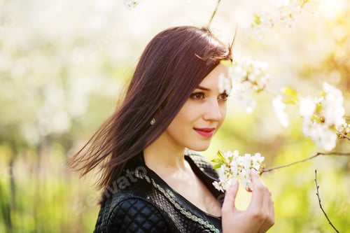 Preview: Close up portrait of young brunette girl with cherry blossom at spring garden.