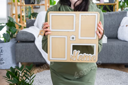 Preview: Happy woman in house holds in hands photo frame with figure at home template and key in interior. Dr