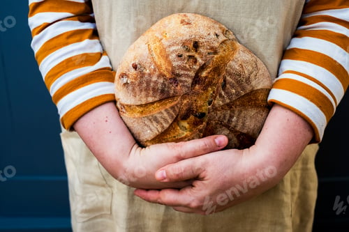 Preview: Close up of person holding a freshly baked round loaf of bread.