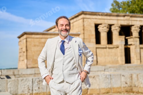 Preview: Smiling man in a striped suit posing near an ancient stone temple outdoors