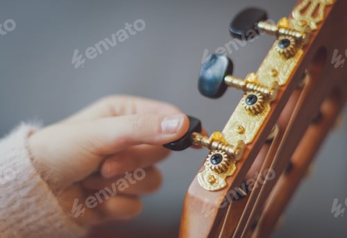 Preview: The girl twists the guitar peg while tuning the strings.