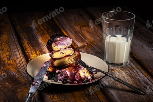 Preview: sliced cheesecakes with blueberry jam and sour cream on a plate with a glass of milk on the table