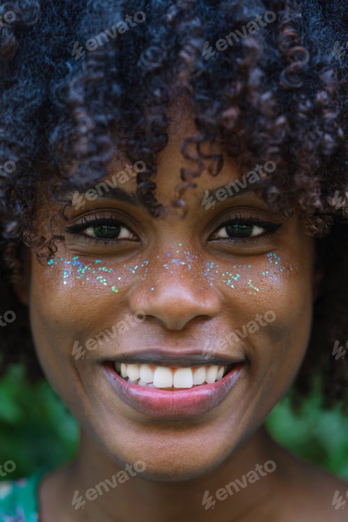Preview: Portrait of the beautiful woman with a dark skin and Afro hair and glitter on her face smiling