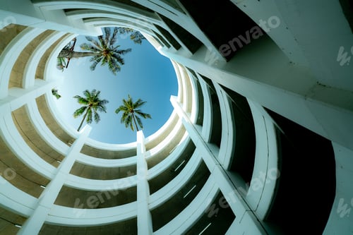 Preview: Bottom view multi-story car park building with coconut tree above building in summer. Multi-level p