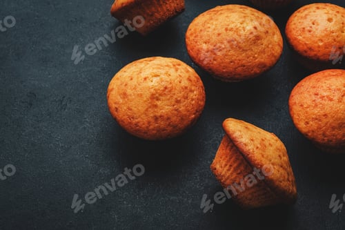 Preview: Appetizing orange muffins or cupcakes on black table background, winter homemade pastries, top view