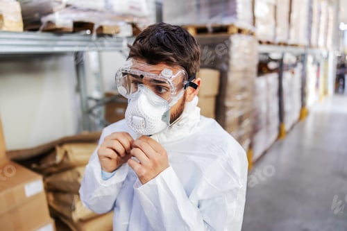Preview: Closeup Of Young Worker In Sterile Uniform And Protective Mask And Glasses On Standing In Warehouse