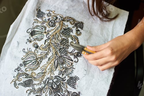 Preview: Woman hands cutting away loose ends of threads from fabric with machine embroidery using scissors.