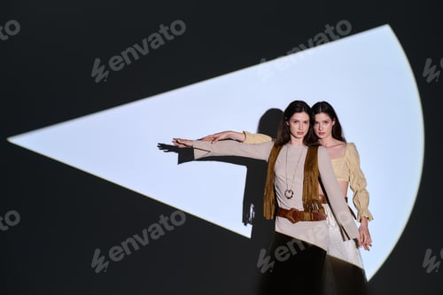 Preview: Elegant twin sisters showcase stylish outfits against a creative backdrop with striking light play