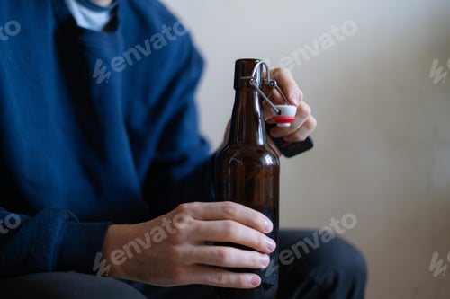 Preview: man holding the glass bottle of alcohol sitting at home in depression, bad habit problem
