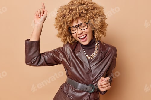 Preview: Energetic curly haired young woman has fun dances carefree moves with rhythm of music wears