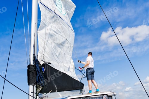 Preview: Raising the sail on a yacht. Young man captan lifting the sail of catamaran yacht during cruising