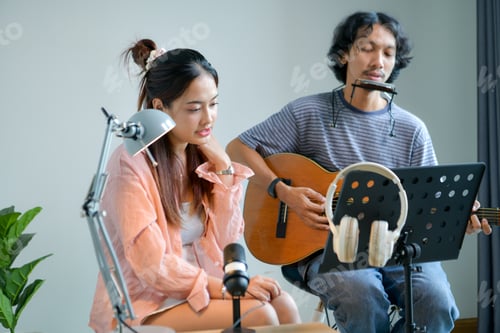 Preview: Happy Asian woman enjoying music with headphones while man plays guitar and harmonica