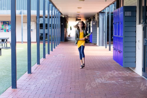 Preview: Caucasian schoolgirl holding books, running in school corridor, with copy space