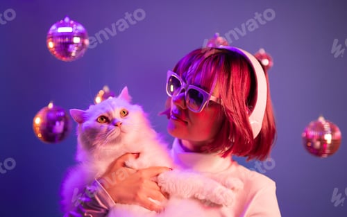 Preview: Gorgeous woman with pink dyed hair listening music in headphones. White cat.