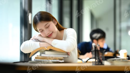 Preview: Young woman resting her head on a stack of books taking a break during study session