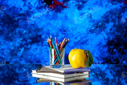 Preview: Front view of colored pencils kept in a glass jar and quince with stem on stacked spiral notebooks