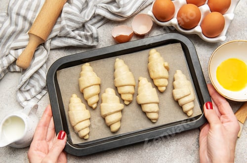 Preview: Baker holding baking tray with freshly made croissants, ready to bake