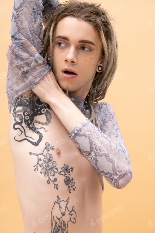 Preview: Tattooed queer person in crop top touching arm isolated on yellow