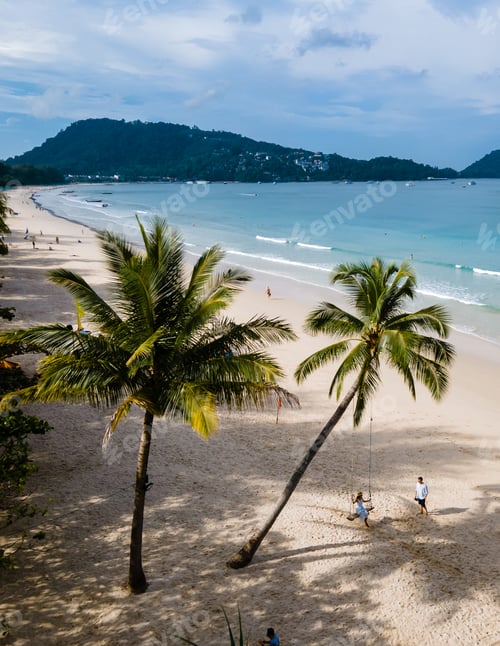 Preview: A couple of men and women on a swing under a palm tree at the beach of Patong Phuket Thailand