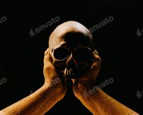 Preview: Hands with human skull on black. Golden sands, time concept. Symbolism, mortality