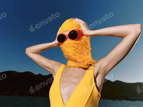 Preview: Woman in yellow dress, sunglasses on head, and furry hat standing by water, exuding summery vibe