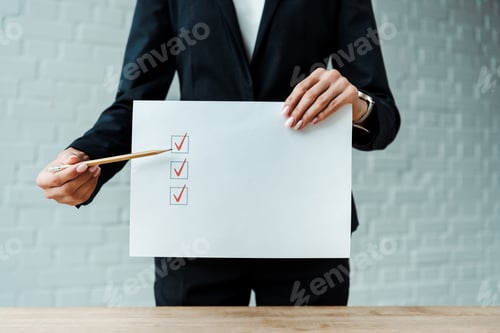 Preview: cropped view of woman holding pencil near paper with check list