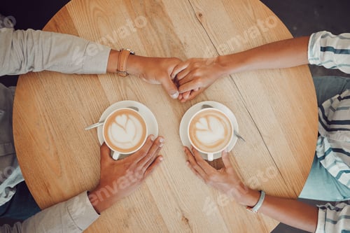 Preview: Close up of young couple in love holding hands with two cups of coffee on a table while sitting in