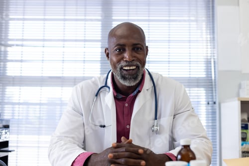 Preview: African american male doctor sitting at desk having video call at doctor's office