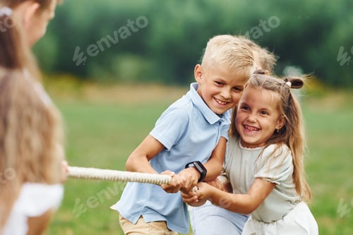 Preview: Smiling, playing tug of war game. Kids are having fun on the field at daytime together