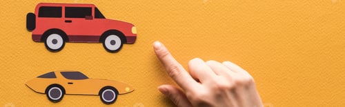 Preview: cropped view of woman pointing with finger at paper cars on orange background, panoramic shot