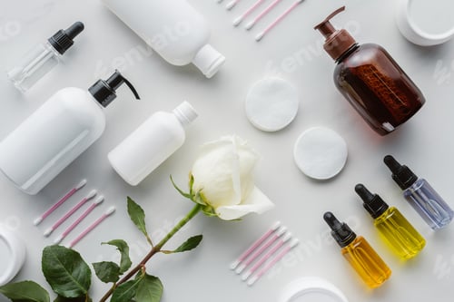 Preview: top view of bottles of cream, cosmetic pads and rose on white surface, beauty concept