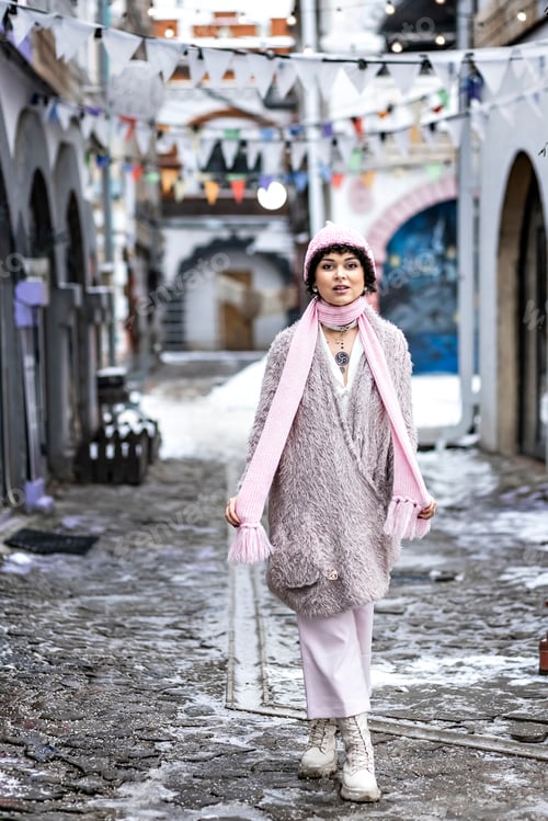 Vorschau: Porträt einer stilvollen jungen Frau in pastellfarbenen warmen Kleidern draußen in der Stadt im Winter