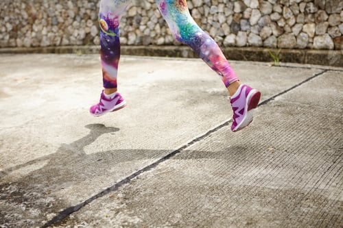 Preview: Freeze action shot of female runner in purple sneakers training outdoors, jogging along concrete pat
