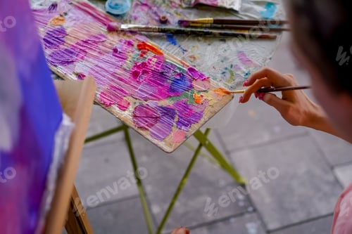 Preview: Close-up of a girl artist with a brush applying oil paint to a painting standing on easel