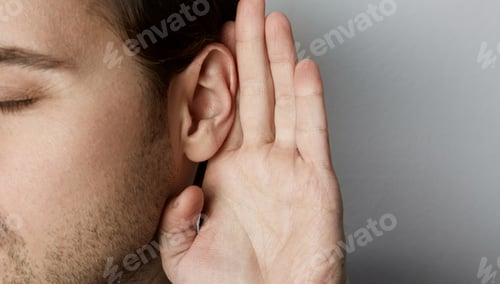 Preview: Listening male holds his hand near his ear over grey background.